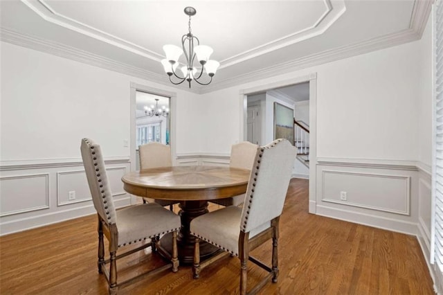 dining room featuring wood finished floors, an inviting chandelier, crown molding, a decorative wall, and a raised ceiling