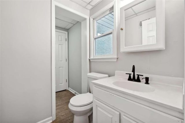 bathroom featuring baseboards, a drop ceiling, toilet, wood finished floors, and vanity