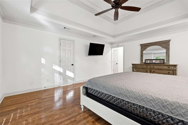 bedroom featuring visible vents, baseboards, a tray ceiling, ornamental molding, and wood finished floors