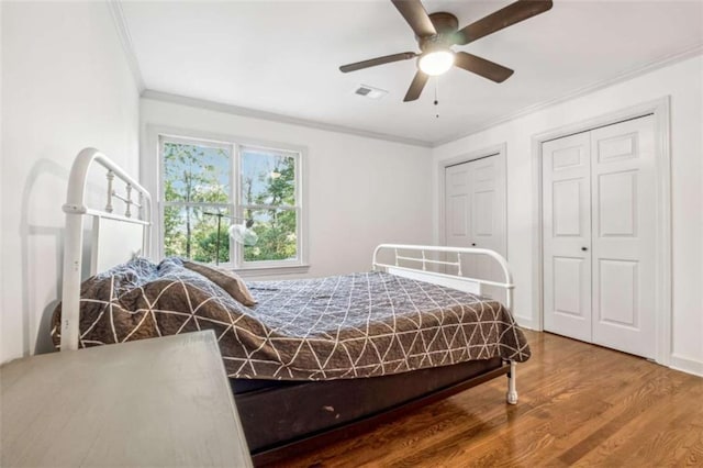 bedroom with a ceiling fan, crown molding, wood finished floors, and visible vents