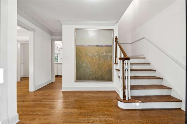 staircase featuring crown molding, wood finished floors, baseboards, and a chandelier