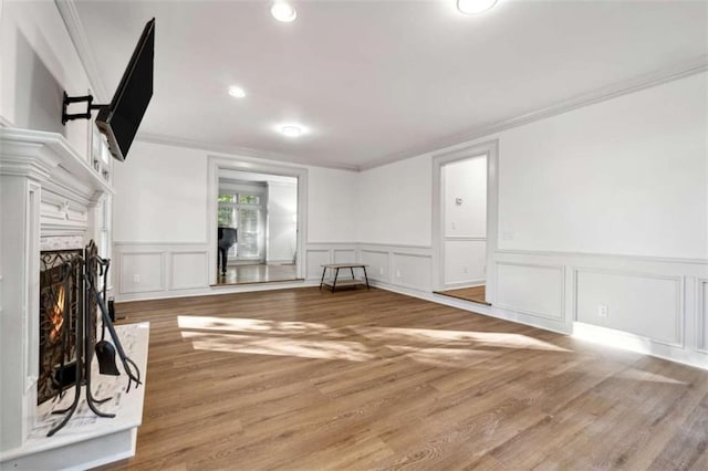 unfurnished living room featuring ornamental molding, a warm lit fireplace, wood finished floors, recessed lighting, and a decorative wall