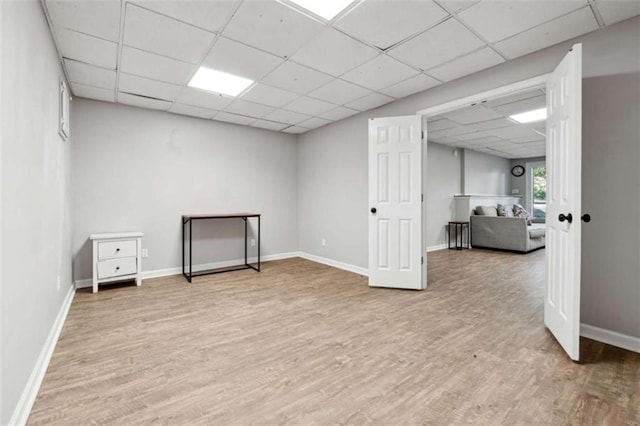 basement with light wood-style flooring, a paneled ceiling, and baseboards