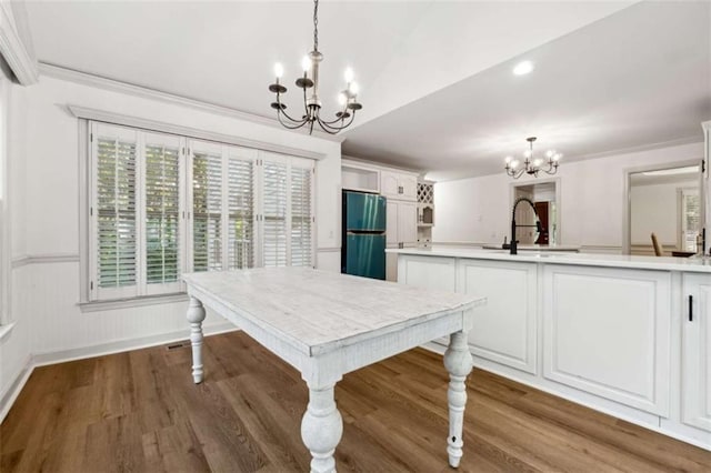 unfurnished dining area with ornamental molding, wainscoting, wood finished floors, a notable chandelier, and a sink