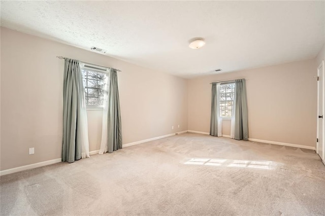 empty room featuring visible vents, light carpet, and baseboards