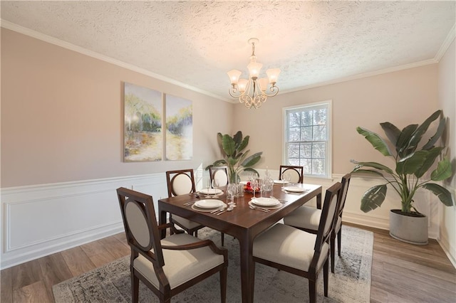 dining room with wainscoting, a textured ceiling, an inviting chandelier, and wood finished floors