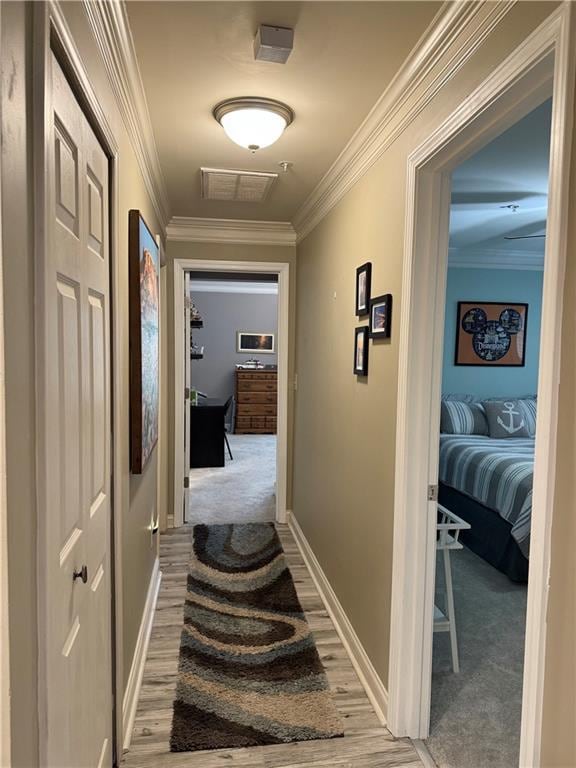 hallway featuring baseboards, visible vents, light wood-style flooring, and ornamental molding