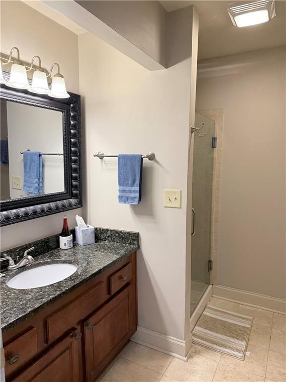 bathroom featuring tile patterned flooring, vanity, a stall shower, and baseboards