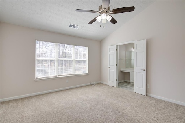 unfurnished bedroom featuring lofted ceiling, a textured ceiling, visible vents, and light colored carpet