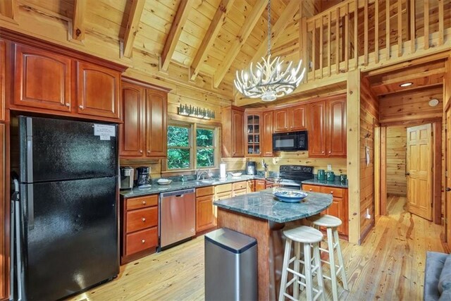 kitchen with black appliances, a kitchen island, wood walls, and hanging light fixtures