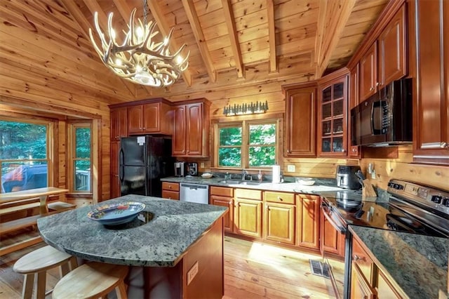 kitchen with black appliances, pendant lighting, wooden walls, and light hardwood / wood-style floors