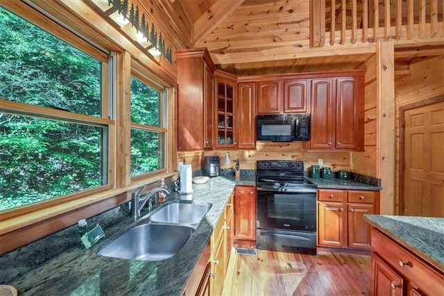 kitchen with black appliances, light hardwood / wood-style floors, sink, dark stone countertops, and wooden walls