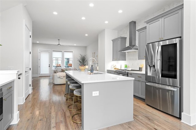 kitchen featuring sink, a kitchen breakfast bar, an island with sink, stainless steel appliances, and wall chimney range hood