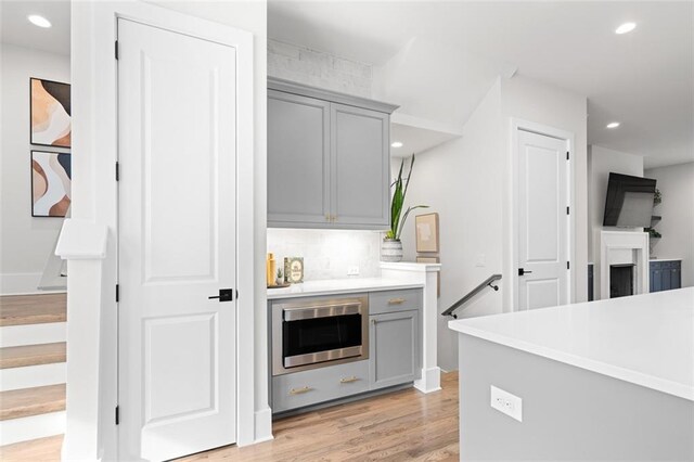 kitchen with gray cabinets, stainless steel microwave, decorative backsplash, and light hardwood / wood-style flooring