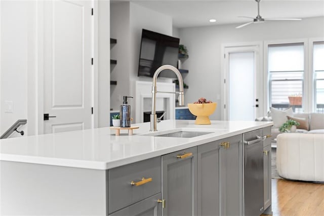 kitchen featuring sink, gray cabinetry, a kitchen island with sink, ceiling fan, and light hardwood / wood-style flooring