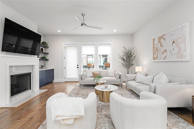 living room featuring ceiling fan, a high end fireplace, and light hardwood / wood-style flooring