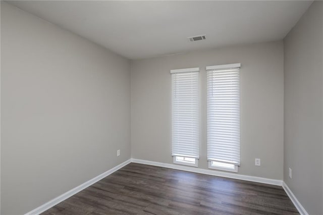 empty room with dark wood-style floors, visible vents, and baseboards