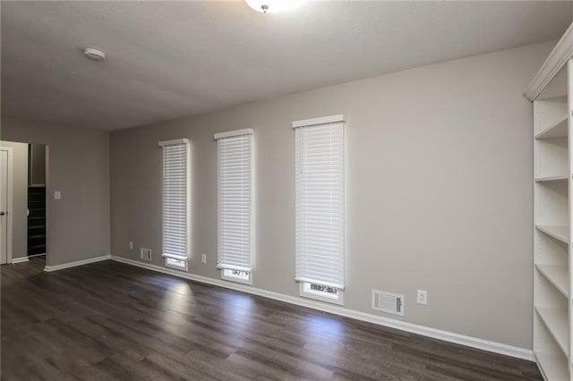 unfurnished room with baseboards, visible vents, and dark wood-style flooring