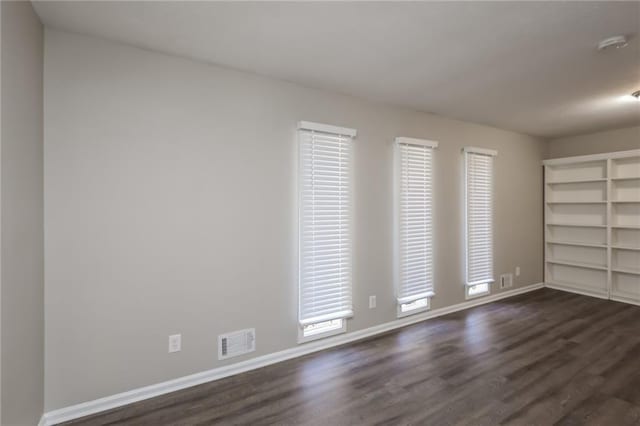 spare room with dark wood-style flooring, visible vents, and baseboards