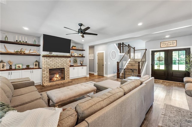 living room with ceiling fan, a brick fireplace, light hardwood / wood-style floors, and french doors