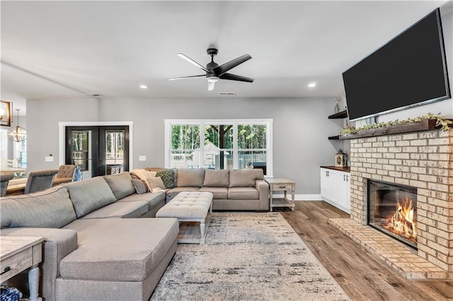 living room featuring hardwood / wood-style flooring, a brick fireplace, ceiling fan, and french doors