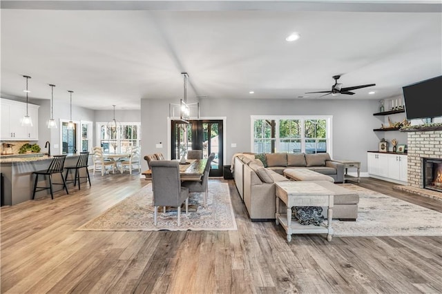 living room with ceiling fan with notable chandelier, a fireplace, and light wood-type flooring