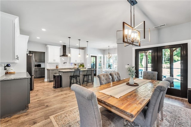 dining room with french doors, plenty of natural light, light wood-type flooring, and a notable chandelier