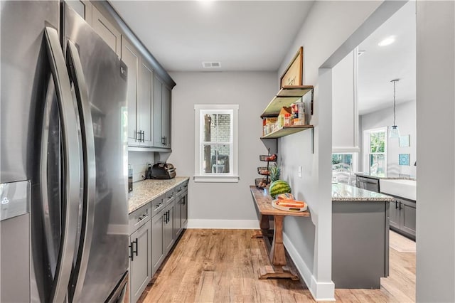 kitchen featuring pendant lighting, gray cabinetry, refrigerator with ice dispenser, light stone counters, and light hardwood / wood-style flooring