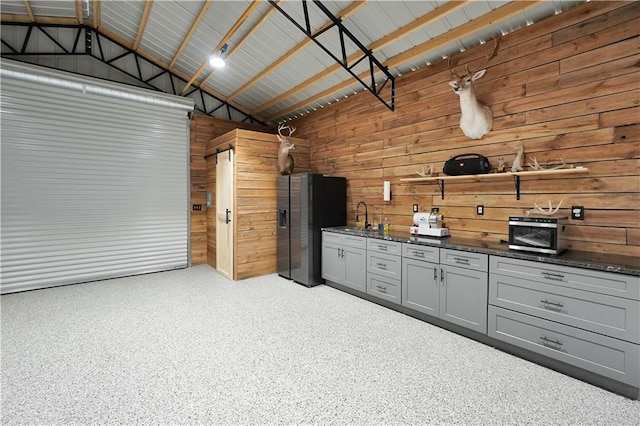 garage with stainless steel fridge with ice dispenser, sink, and wooden walls