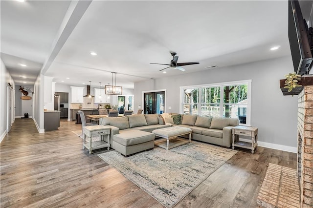 living room featuring wood-type flooring, ceiling fan with notable chandelier, and a fireplace