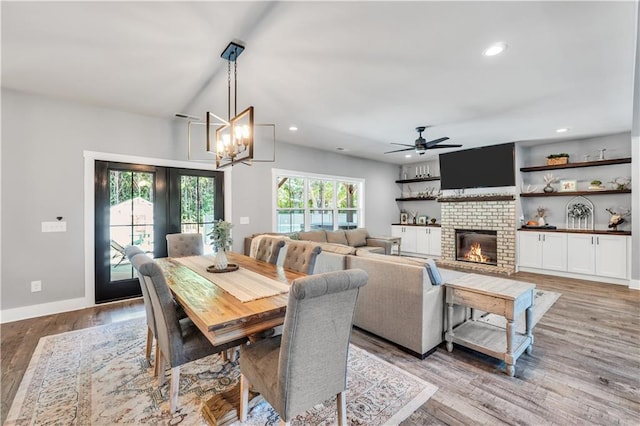 dining space featuring ceiling fan with notable chandelier, a fireplace, light wood-type flooring, and a wealth of natural light