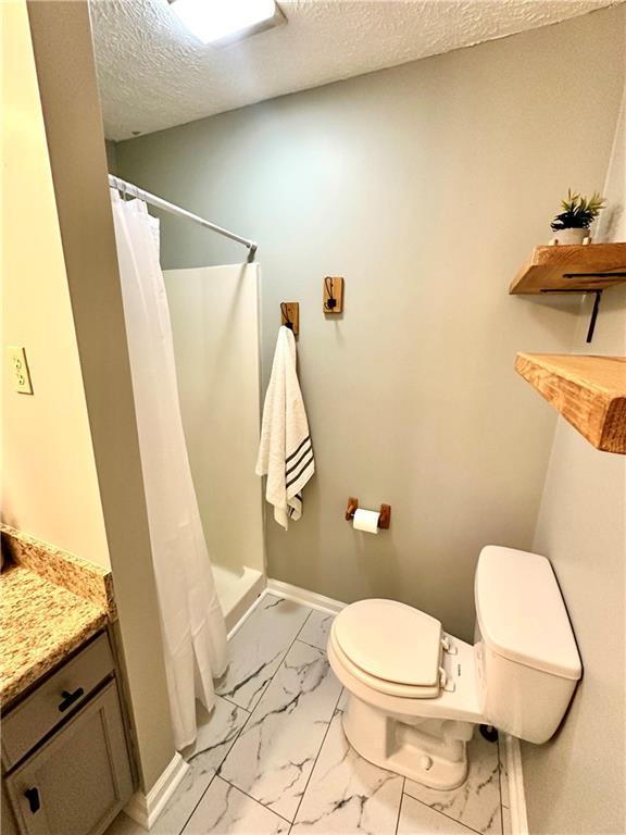bathroom featuring marble finish floor, toilet, a shower with curtain, and a textured ceiling