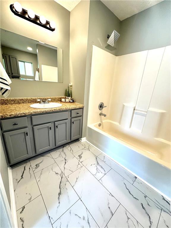full bath with marble finish floor, baseboards, vanity, and tub / shower combination