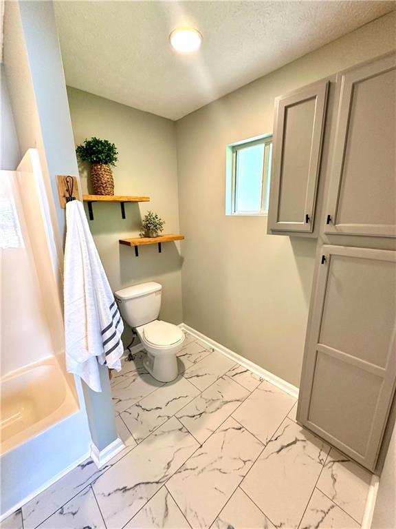 full bath featuring a bath, a textured ceiling, toilet, baseboards, and marble finish floor