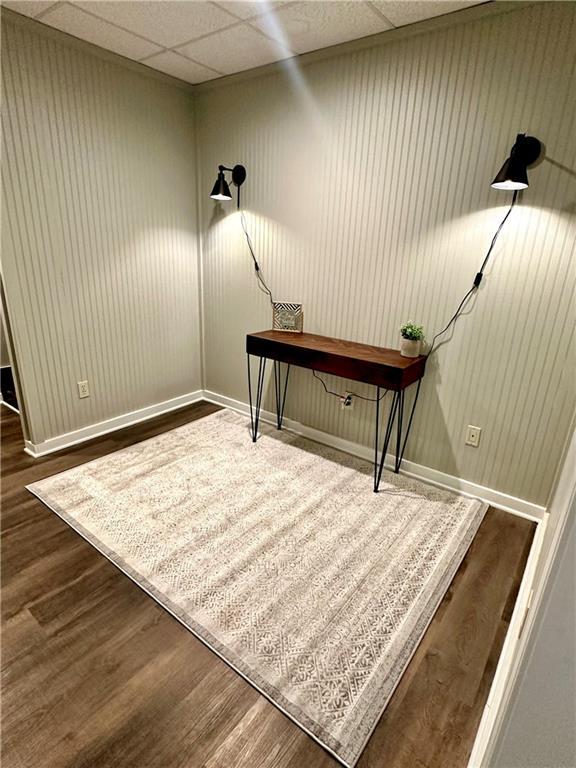 unfurnished office featuring baseboards, wood finished floors, and a drop ceiling