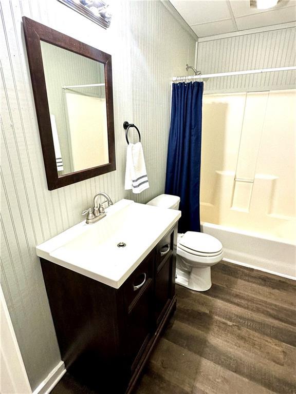 full bath featuring wood finished floors, vanity, wooden walls, shower / bath combination with curtain, and toilet