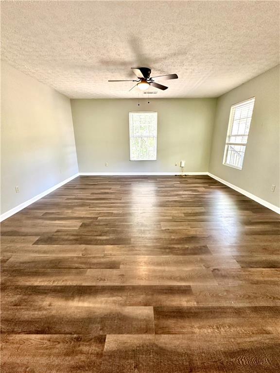 unfurnished room with baseboards, a ceiling fan, dark wood-style floors, and a textured ceiling