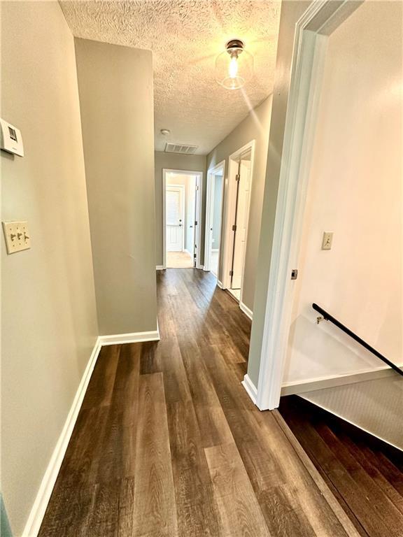 hallway with wood finished floors, a textured ceiling, baseboards, and visible vents