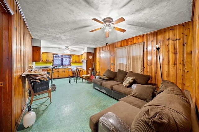 living room with ceiling fan, a textured ceiling, and wooden walls