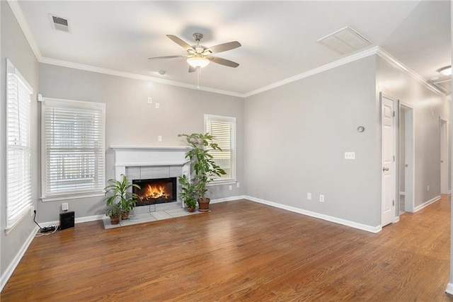 unfurnished living room with ceiling fan, hardwood / wood-style flooring, a tiled fireplace, and crown molding