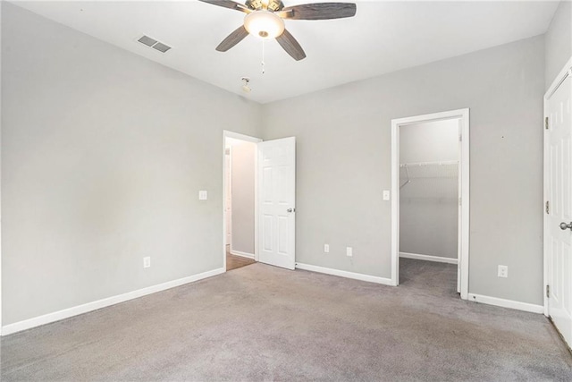 unfurnished bedroom with a spacious closet, ceiling fan, light colored carpet, and a closet