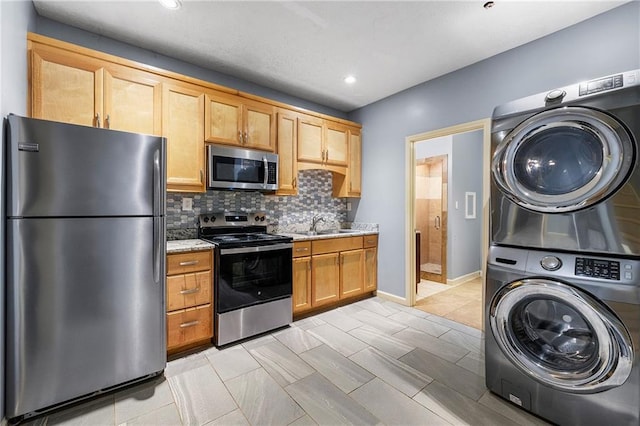 kitchen featuring light stone countertops, sink, stacked washing maching and dryer, stainless steel appliances, and decorative backsplash