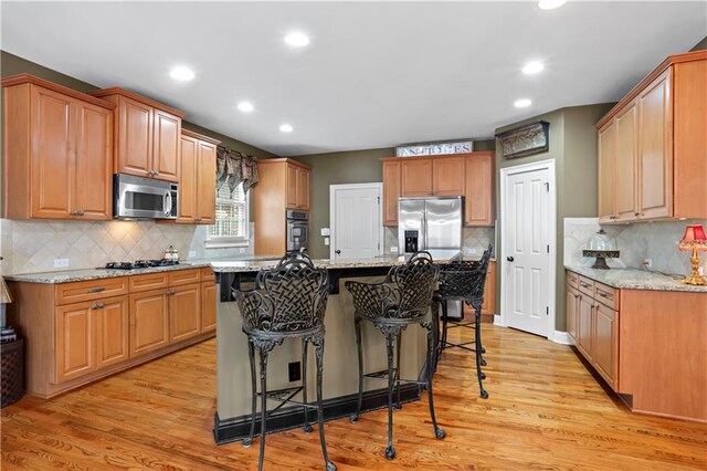 kitchen with stainless steel appliances, light wood finished floors, a breakfast bar, and light stone counters