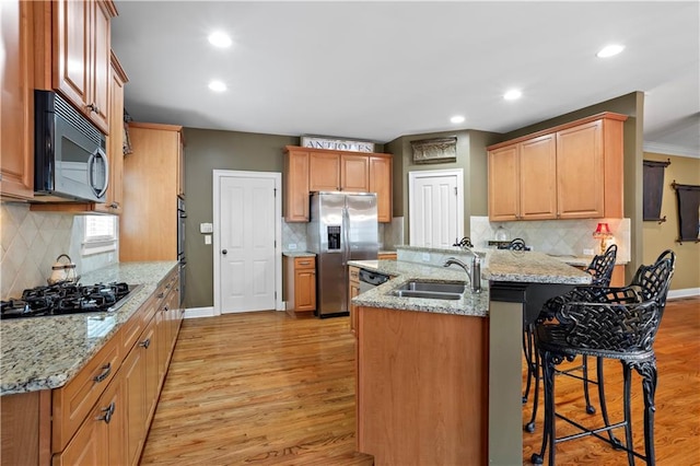 kitchen featuring black gas cooktop, a breakfast bar area, a sink, light wood-style floors, and stainless steel fridge with ice dispenser