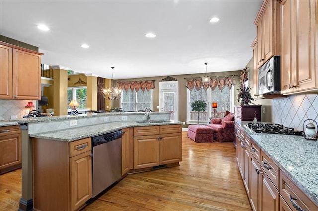 kitchen with appliances with stainless steel finishes, a sink, light wood-style flooring, and an inviting chandelier