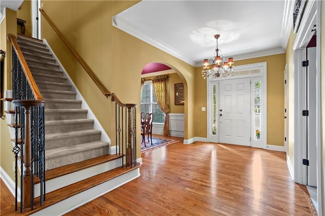 entryway featuring a chandelier, arched walkways, ornamental molding, and wood finished floors