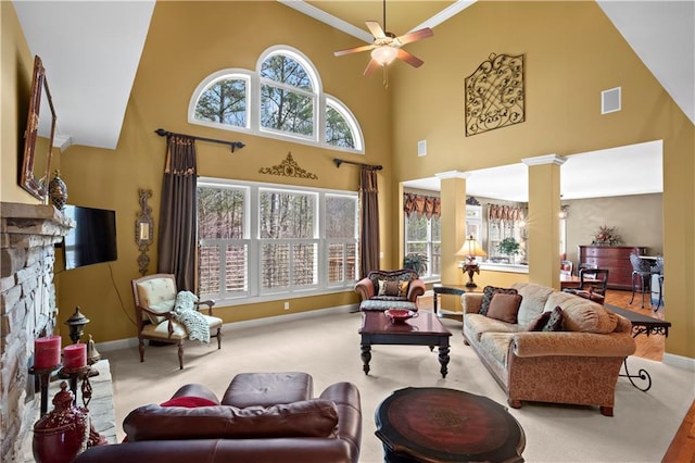 carpeted living room featuring visible vents, baseboards, ceiling fan, a stone fireplace, and ornate columns