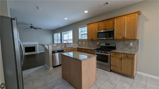 kitchen with stainless steel appliances, sink, a kitchen island, ceiling fan, and light tile patterned flooring