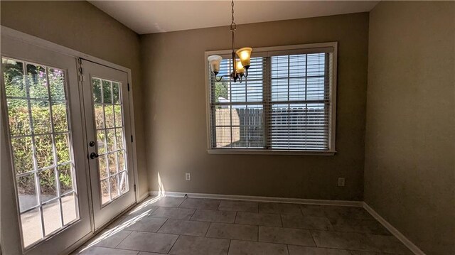 unfurnished dining area with a wealth of natural light, an inviting chandelier, dark tile patterned floors, and french doors