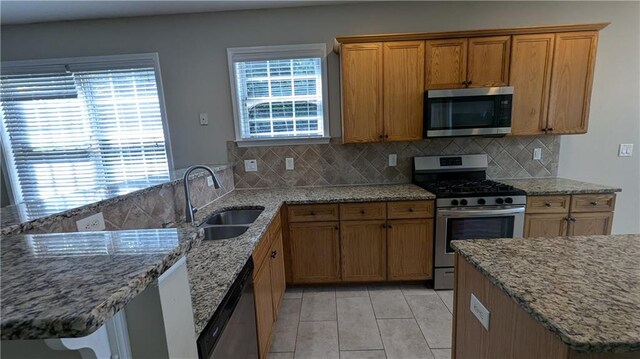 kitchen with appliances with stainless steel finishes, sink, decorative backsplash, and light stone counters